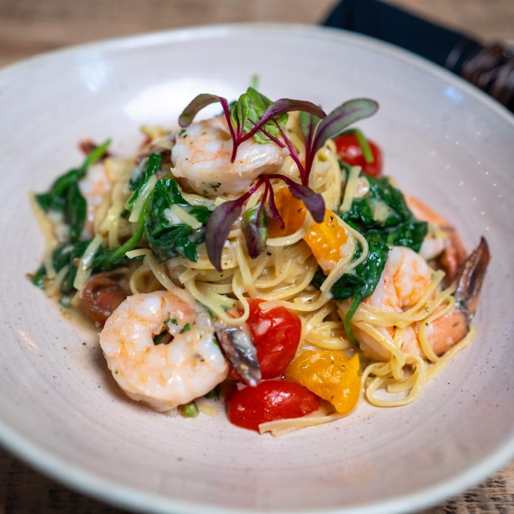 Shrimp pasta with linguine, cherry tomatoes, spinach, and microgreens on a light plate.