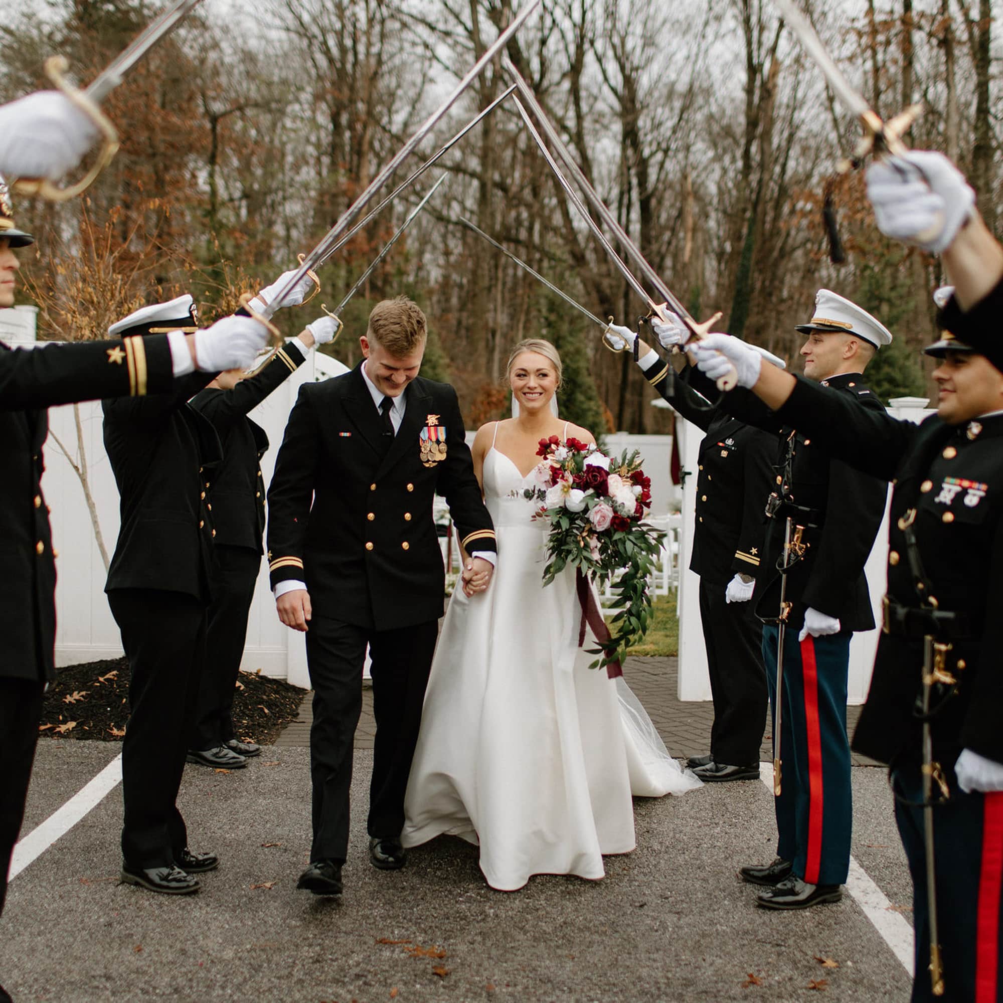 Bride and groom walk beneath a ceremonial sword arch formed by uniformed soldiers at an outdoor wedding.