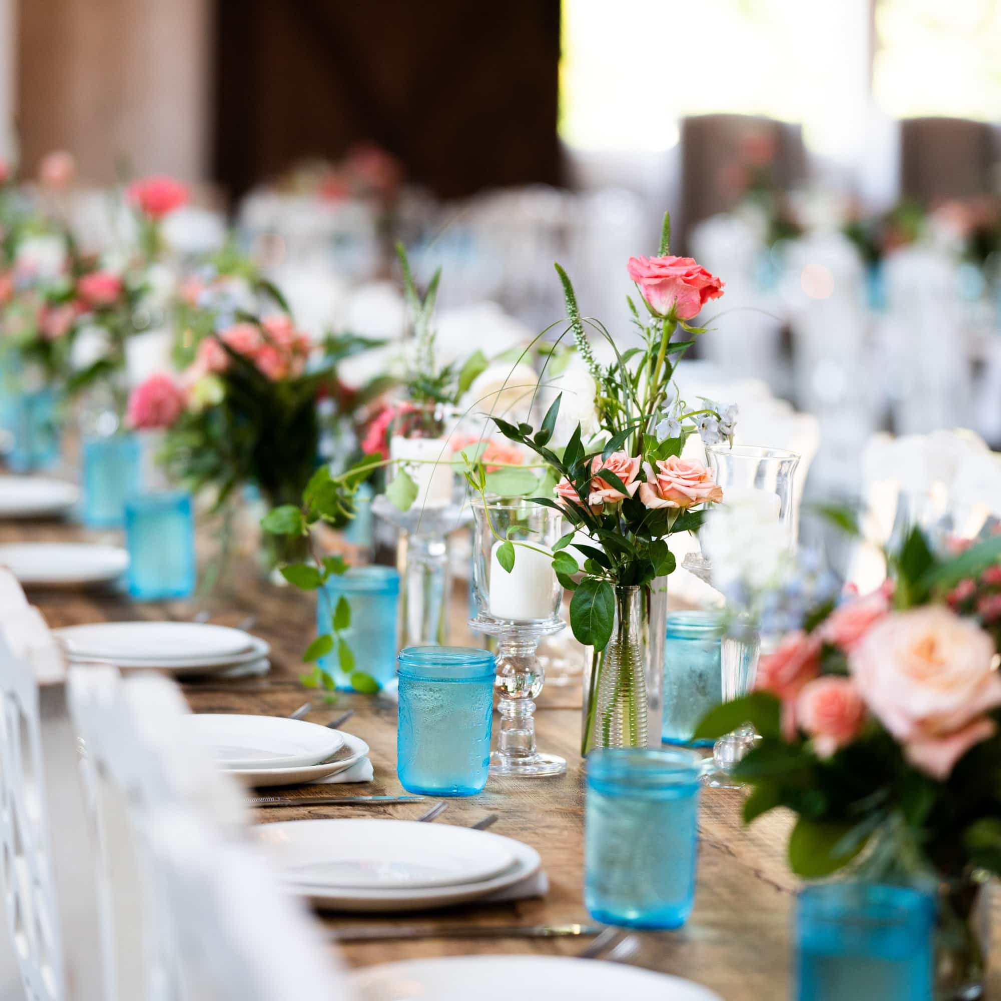 Table set for a formal event with pink roses in glass vases and blue-tinted glasses as part of the centerpiece